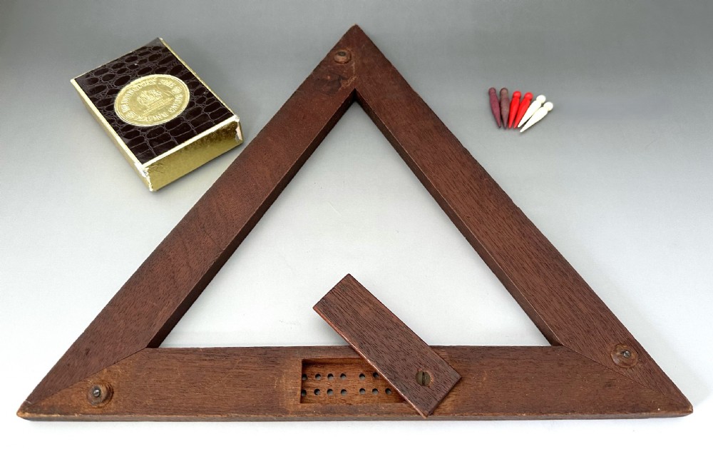 A mid-Victorian triangular wooden cribbage board with geometric inlaid borders, inset white scoring tracks, six coloured pegs, and a playing card box. View II
