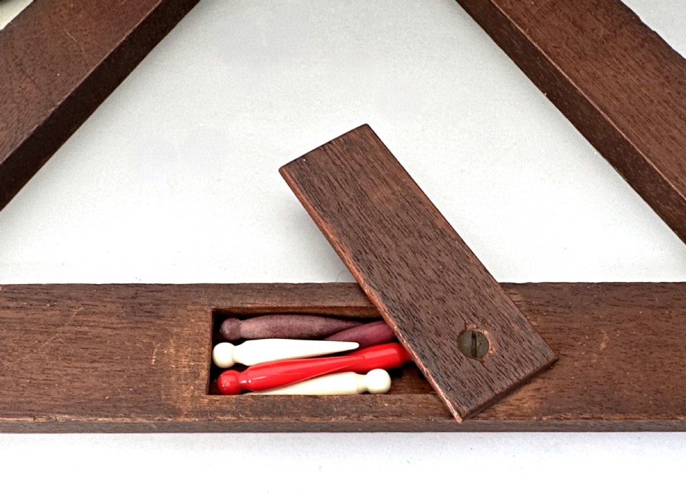 A mid-Victorian triangular wooden cribbage board with geometric inlaid borders, inset white scoring tracks, six coloured pegs, and a playing card box. View III
