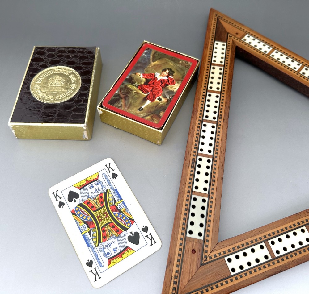 A mid-Victorian triangular wooden cribbage board with geometric inlaid borders, inset white scoring tracks, six coloured pegs, and a playing card box. View IV