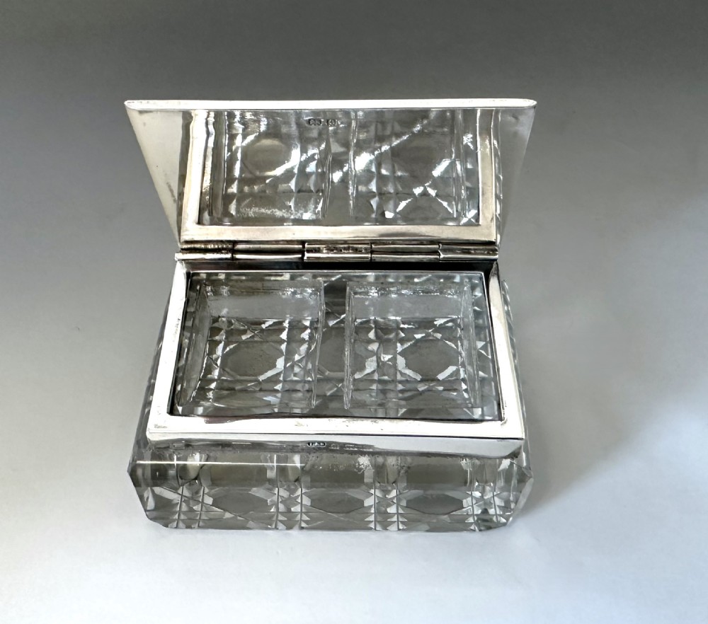 An Edwardian rectangular cut glass stamp box topped with a smooth sterling silver lid showing hallmarks along the rim. View IV