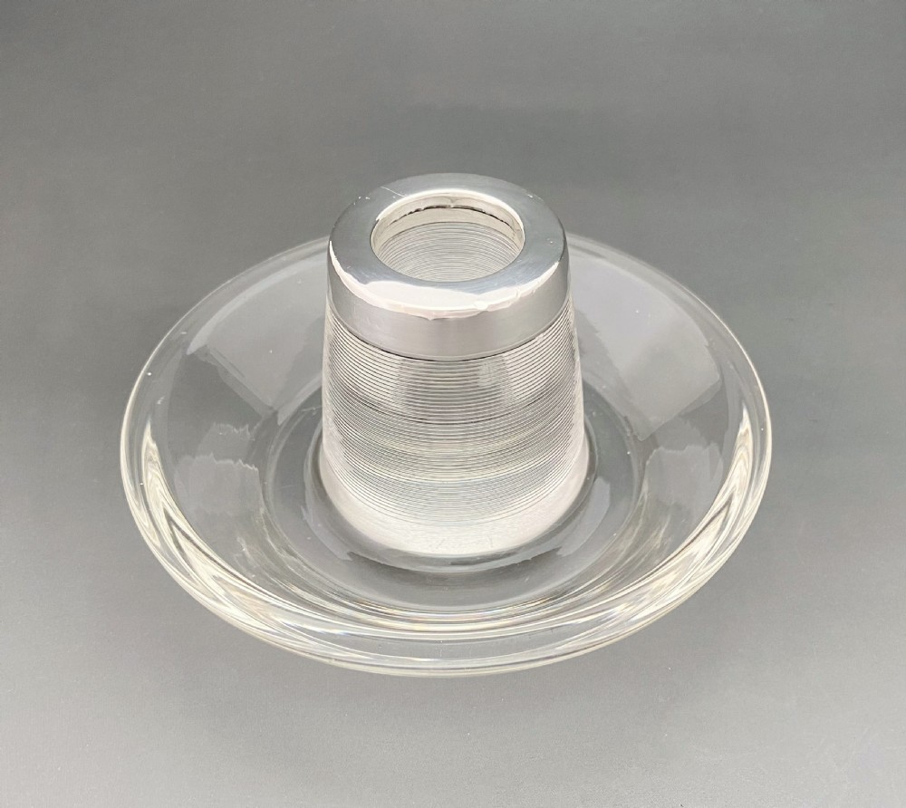 An Edwardian clear glass match striker featuring a ribbed cylindrical body, wide saucer base, and a hallmarked sterling silver collar holding red-tipped matches. View VI
