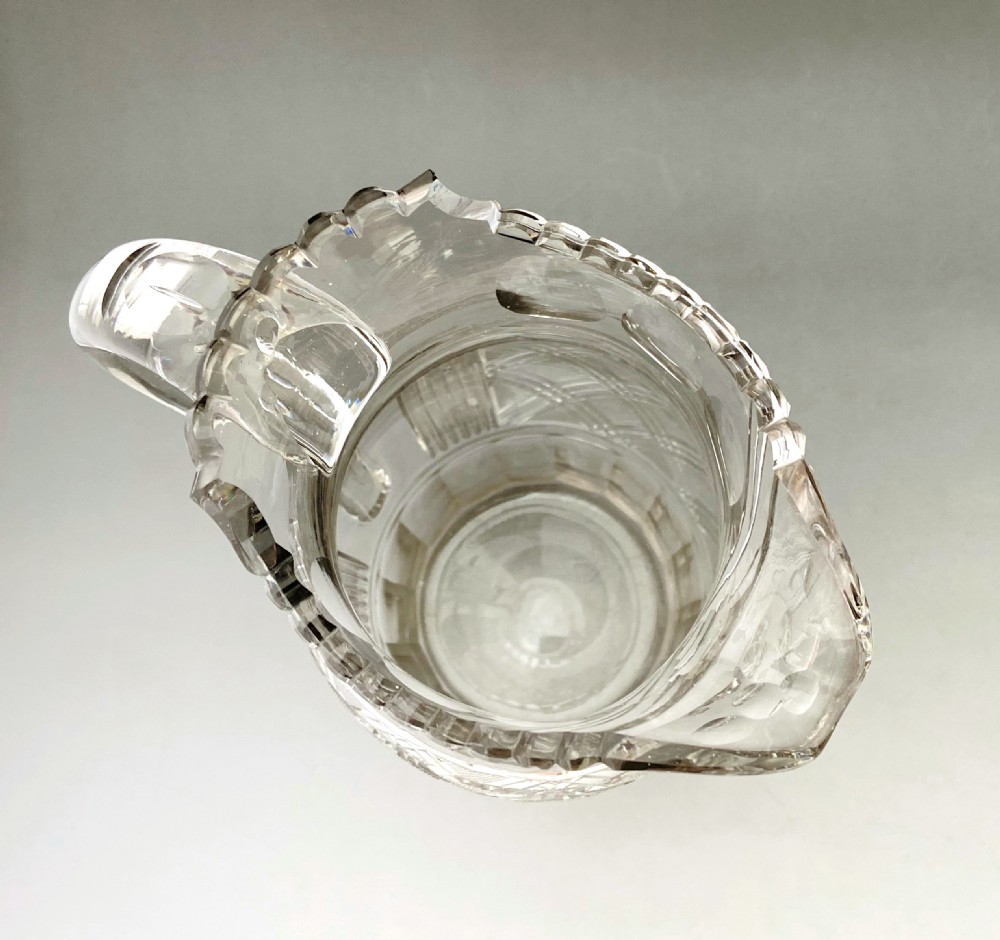 A clear Regency cut lead glass jug featuring diamond-pattern relief carving, a scalloped rim, and a thick curved handle. View VI