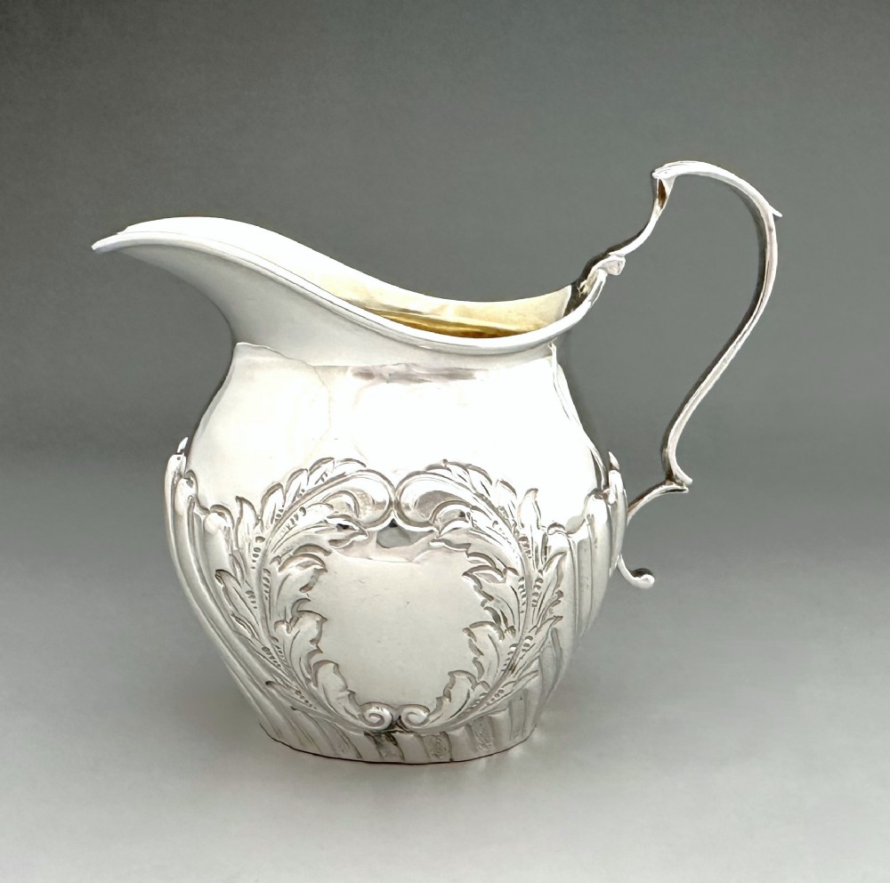 A Victorian silver cream jug featuring chased acanthus leaf motifs, a swept scroll handle, fluted lower body, and a gilt interior.