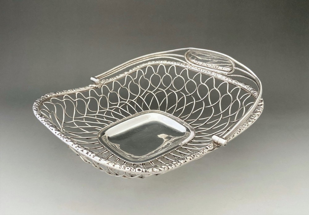 A Georgian silver-plated wirework basket featuring an arched swing handle, open lattice sides, and a polished solid central base. View II