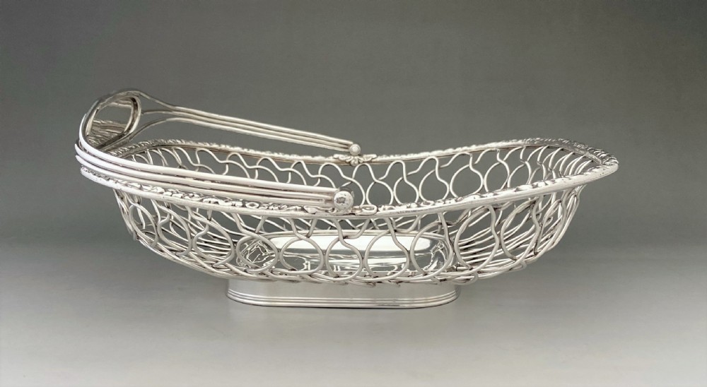 A Georgian silver-plated wirework basket featuring an arched swing handle, open lattice sides, and a polished solid central base. View III