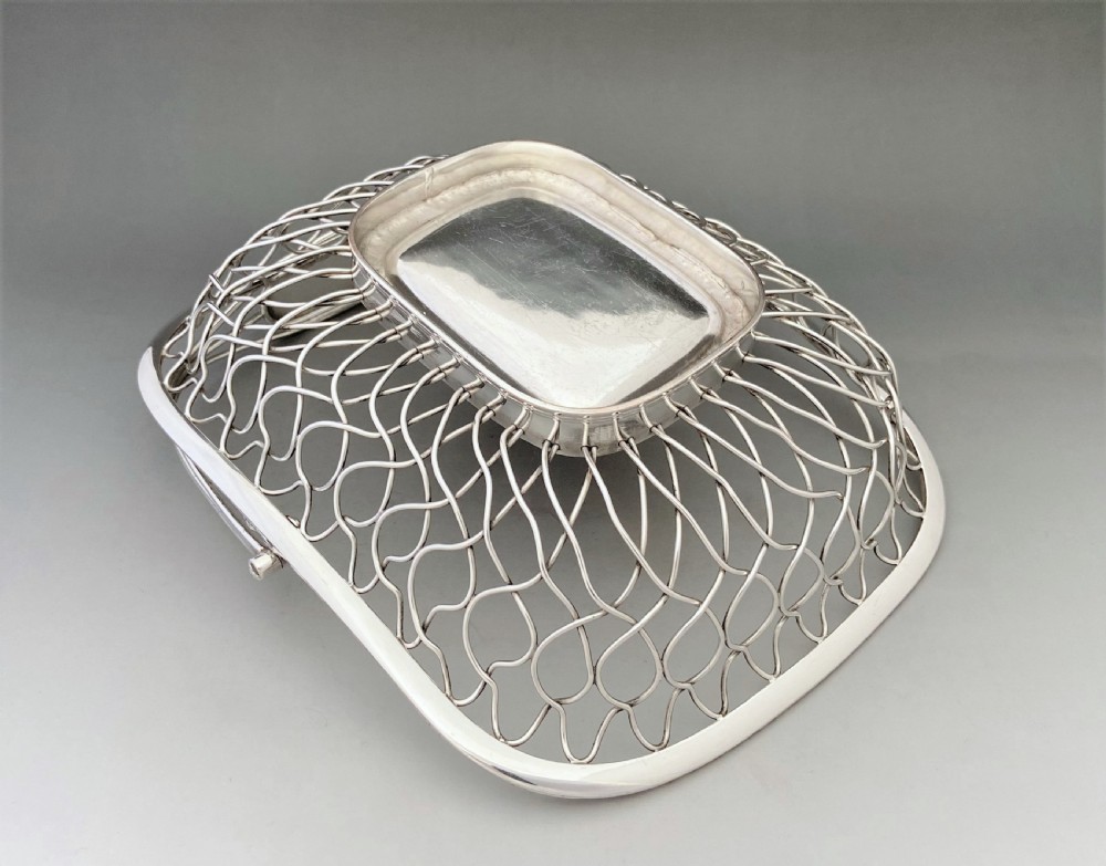 A Georgian silver-plated wirework basket featuring an arched swing handle, open lattice sides, and a polished solid central base. View VII