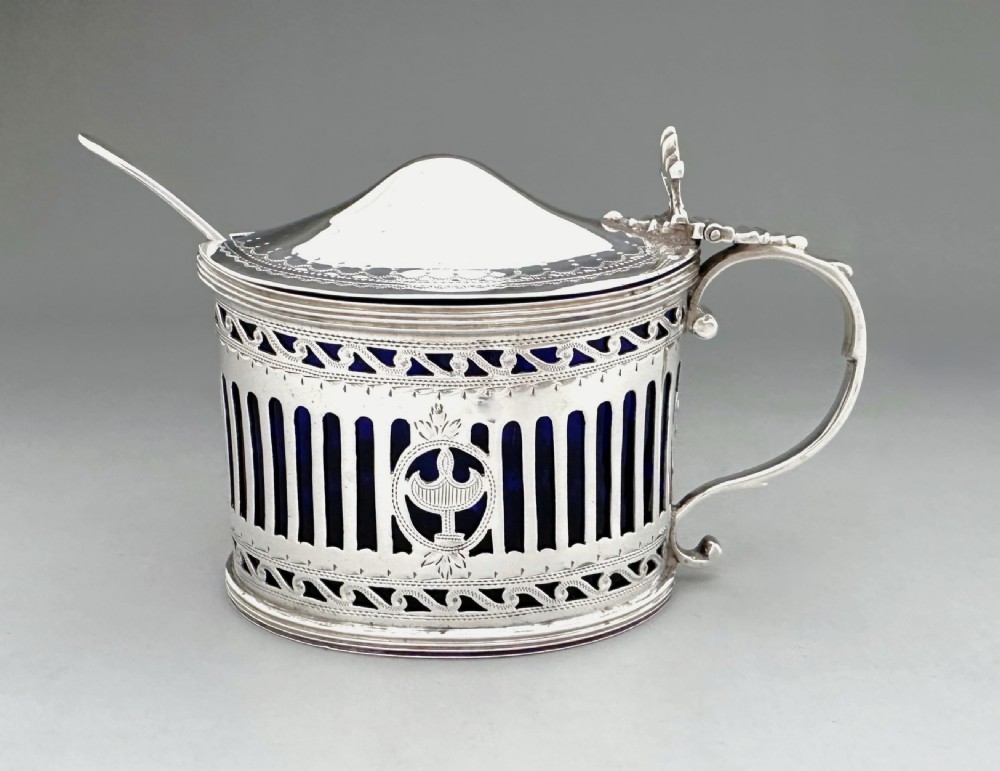 Victorian pierced sterling silver mustard pot with a domed hinged lid, scroll handle, and cobalt blue glass liner.