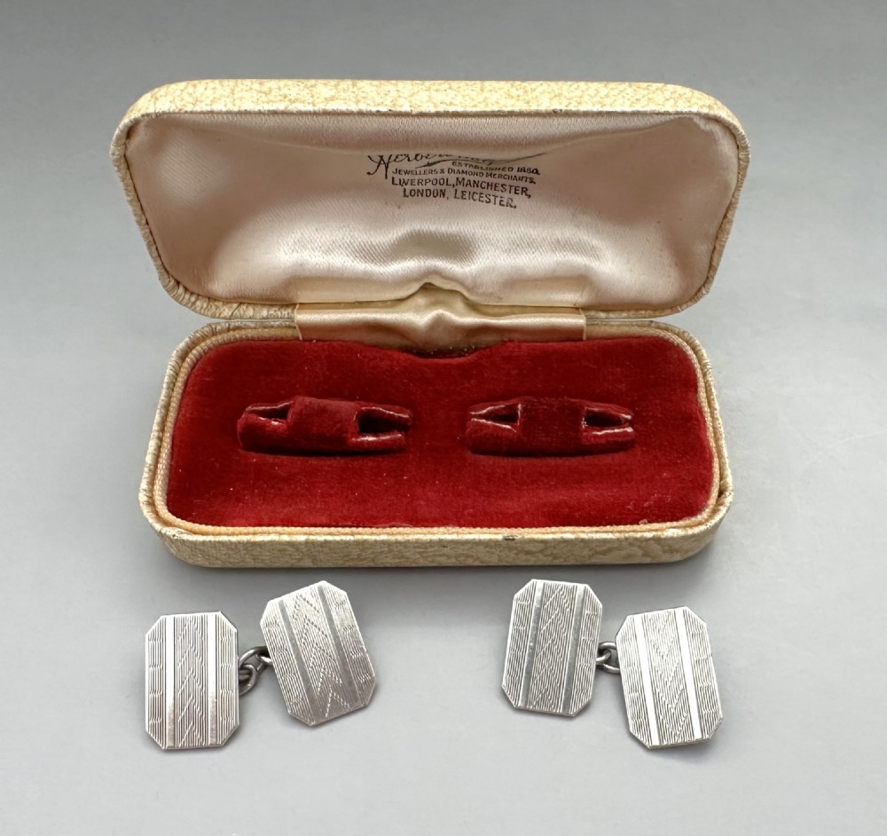 A pair of rectangular silver cufflinks with geometric engine-turned engraving displayed inside a cream fitted presentation box with red velvet lining. View III