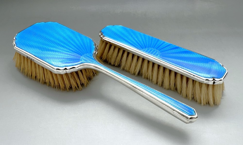 A pair of Art Deco silver vanity brushes featuring bright blue sunburst guilloche enamel panels and natural light bristles. View II
