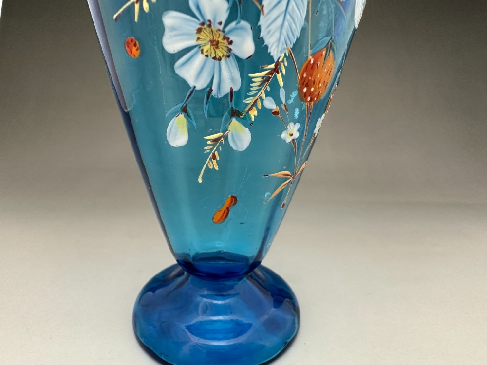 A blue glass vase featuring a flared rim, round pedestal base, and hand-painted enamel floral motifs with wild strawberries. View V