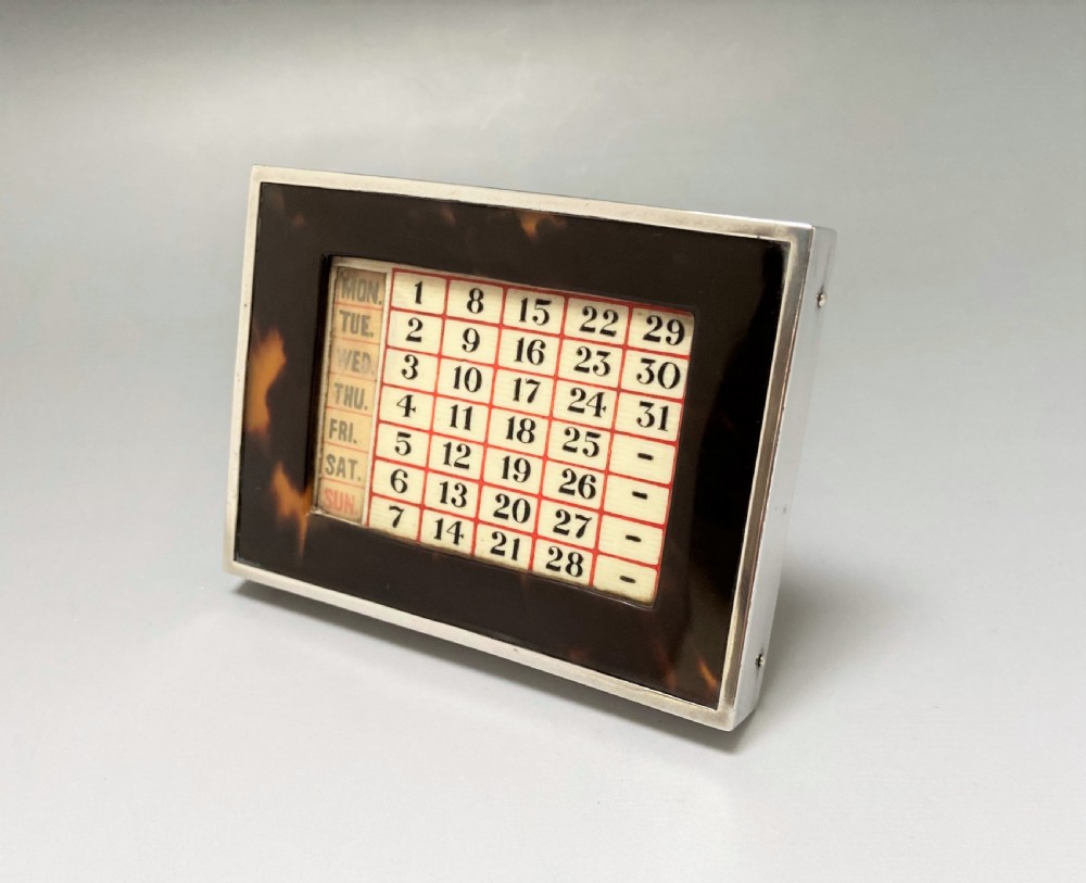 An Art Deco perpetual desk calendar framed in silver with a tortoiseshell border surrounding a central grid displaying printed numbers and days of the week. View II