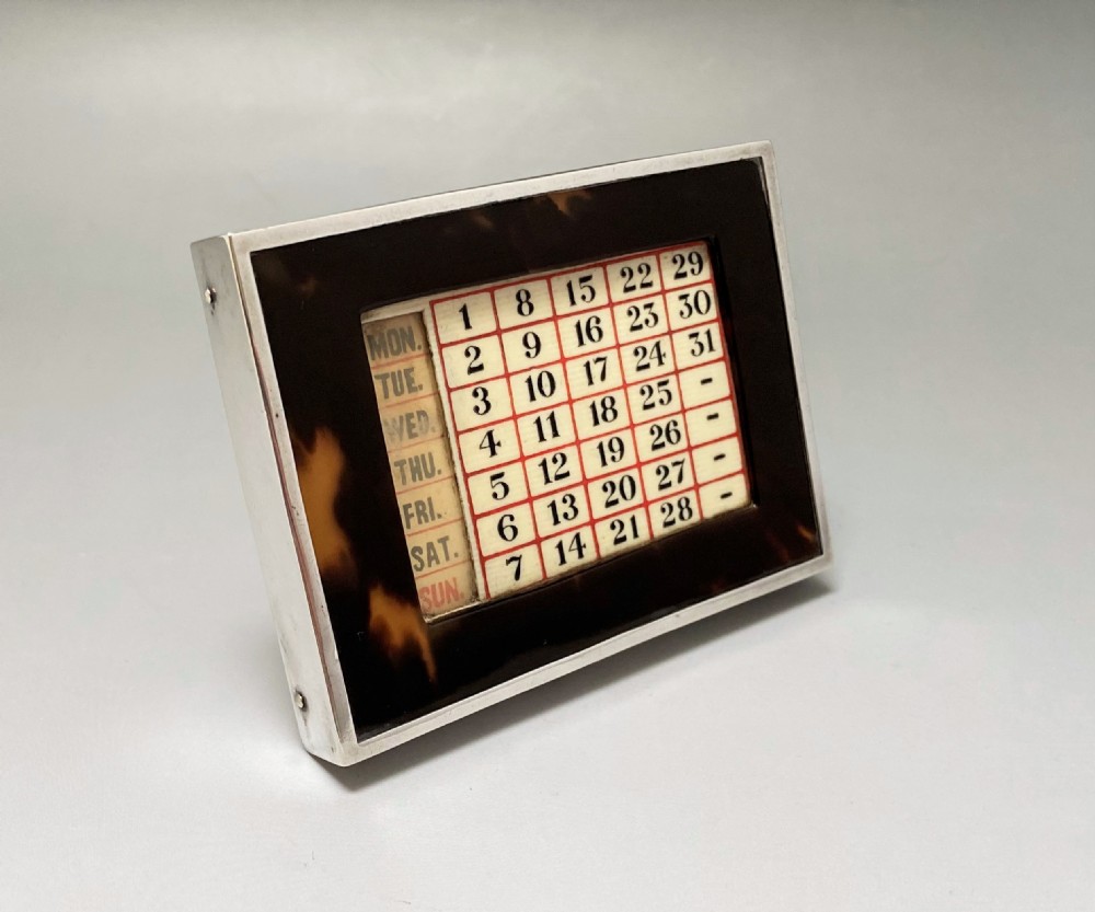 An Art Deco perpetual desk calendar framed in silver with a tortoiseshell border surrounding a central grid displaying printed numbers and days of the week.