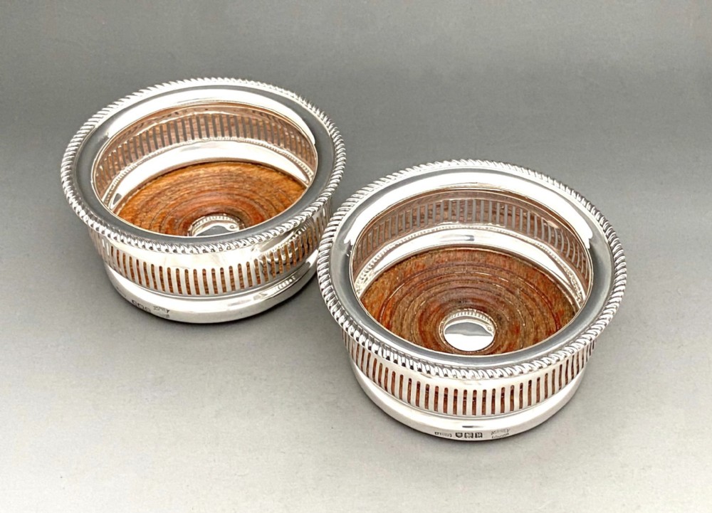 A pair of circular sterling silver wine coasters with pierced side galleries, gadrooned rims, and turned wood bases with central silver buttons.