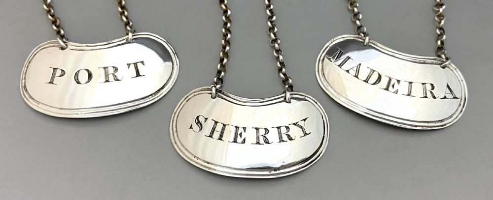 A set of three crescent shaped sterling silver decanter labels with chains, engraved with the words Port, Sherry, and Madeira. View II