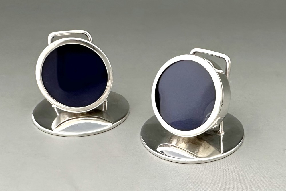 A pair of circular silver menu holders featuring deep blue enamelled centres set on flat round bases.
