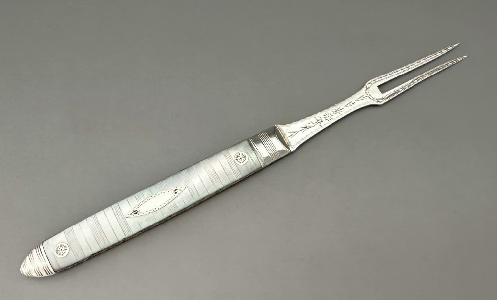 A late eighteenth-century silver folding fruit fork featuring engraved two-pronged tines and a decorated mother-of-pearl handle on a neutral background. View II