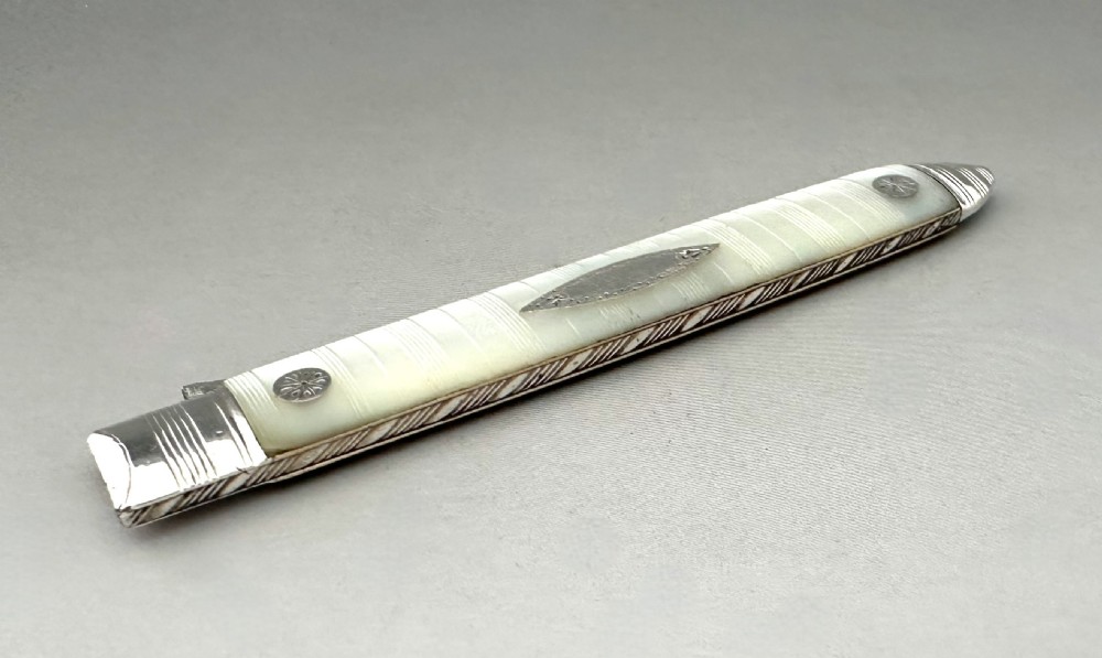 A late eighteenth-century silver folding fruit fork featuring engraved two-pronged tines and a decorated mother-of-pearl handle on a neutral background. View X