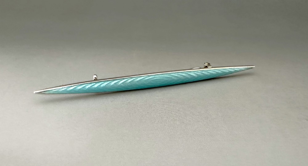 A slender Norwegian sterling silver bar brooch featuring light turquoise guilloche vitreous enamel over an engine-turned pattern.