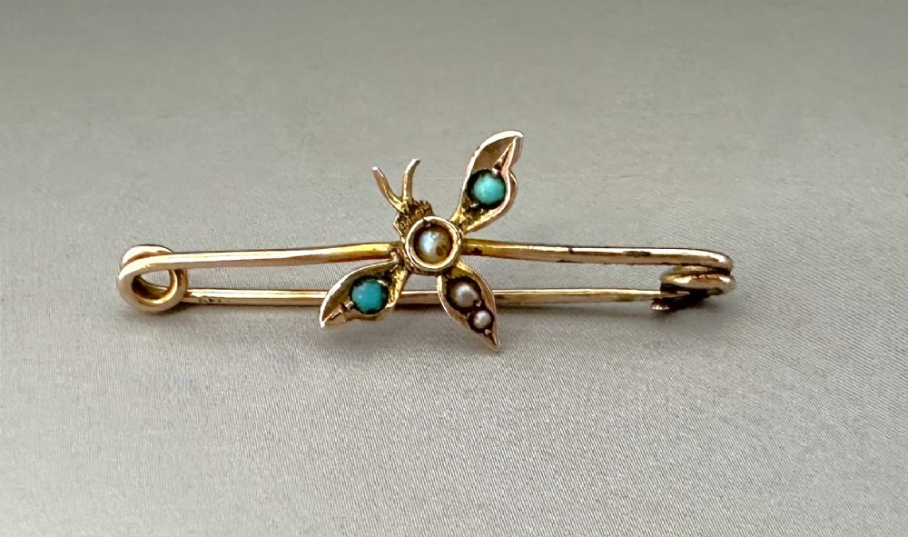 A Victorian 9ct gold safety-pin style bar brooch featuring a stylised dragonfly motif set with turquoise and seed pearls.