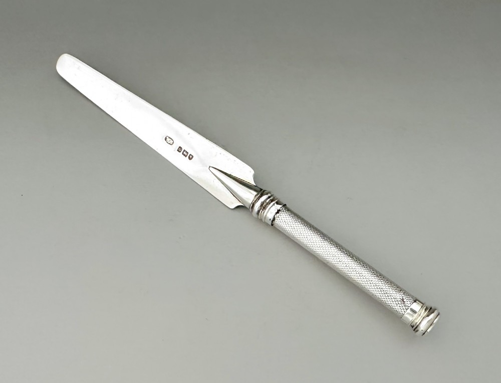 An Edwardian sterling silver letter opener featuring a flat tapered blade stamped with hallmarks and a textured engine-turned handle.