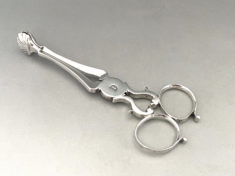 A pair of 18th-century silver scissor-action sugar nips with shell-shaped grips and an engraved monogram on the central pivot.