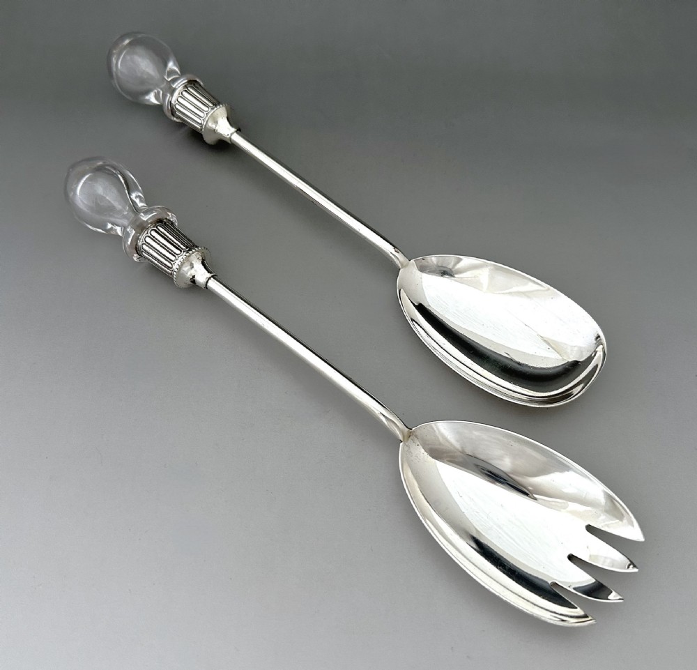 A pair of Edwardian silver salad servers featuring a rounded spoon and a three-pronged fork with decorative fluted ferrules and clear glass drop handles. View V