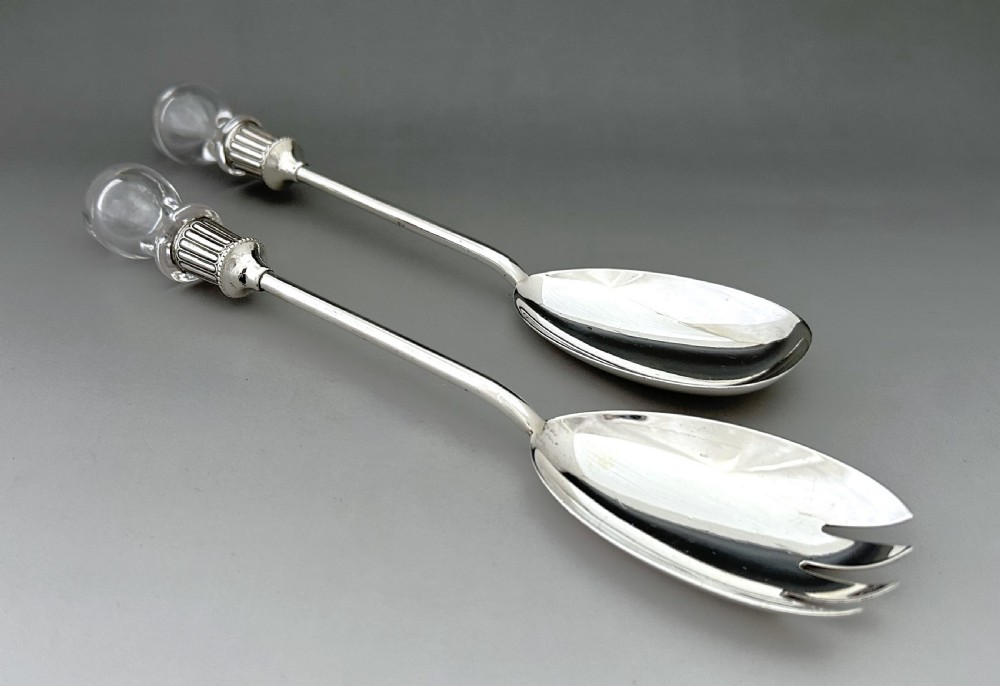 A pair of Edwardian silver salad servers featuring a rounded spoon and a three-pronged fork with decorative fluted ferrules and clear glass drop handles. View VI