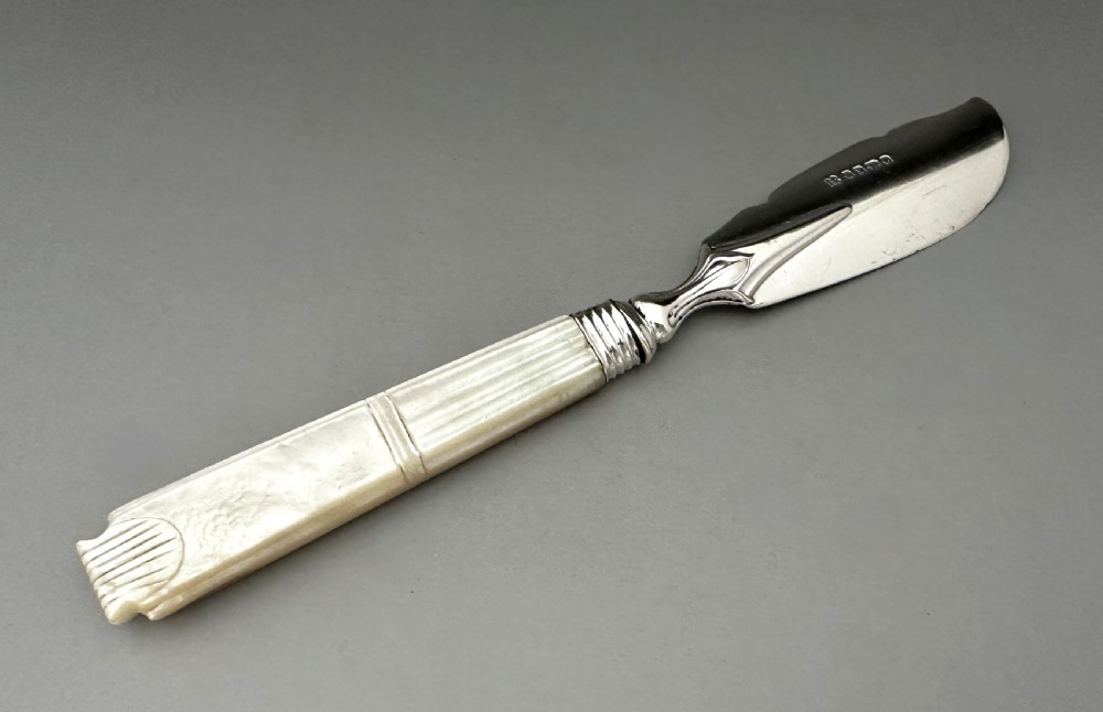 A Victorian silver butter knife featuring an engraved foliate blade and a carved mother-of-pearl handle. View V