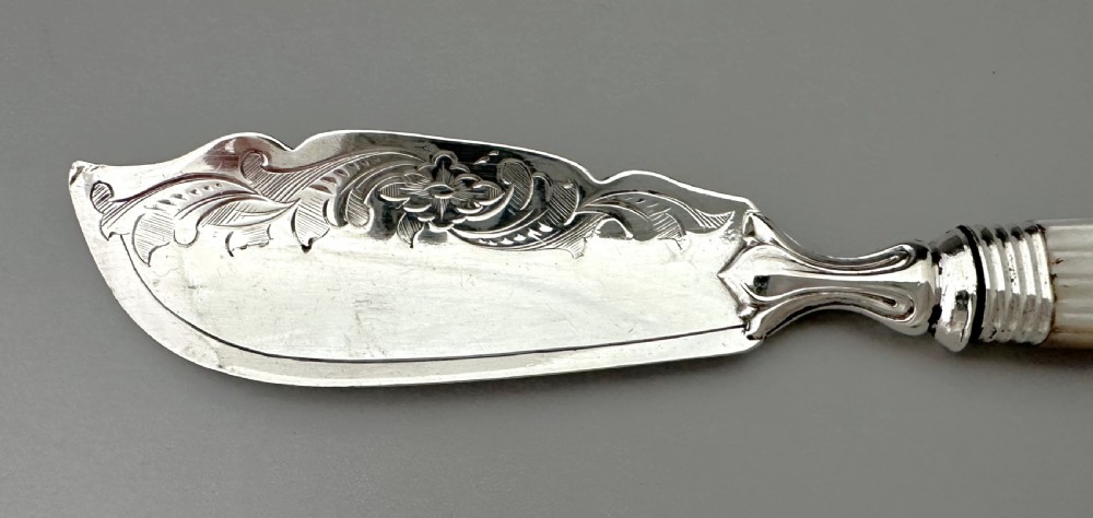 A Victorian silver butter knife featuring an engraved foliate blade and a carved mother-of-pearl handle. View VI