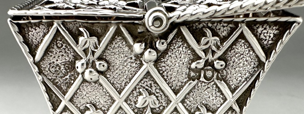 A small Victorian silver potpourri basket featuring a twisted wire handle, lattice-patterned sides, and a pierced floral hinged lid. View X