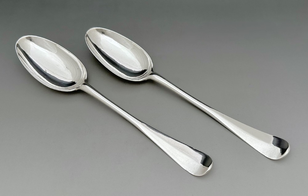 A pair of polished mid-18th-century Scottish sterling silver serving spoons with smooth oval bowls and slender stems resting on a neutral background.
