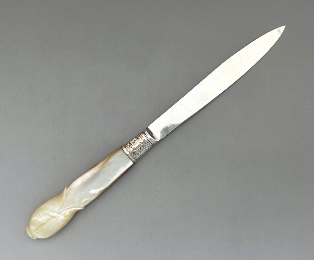 An antique George V letter opener featuring a tapered silver blade, an engraved silver collar, and a carved mother-of-pearl handle.