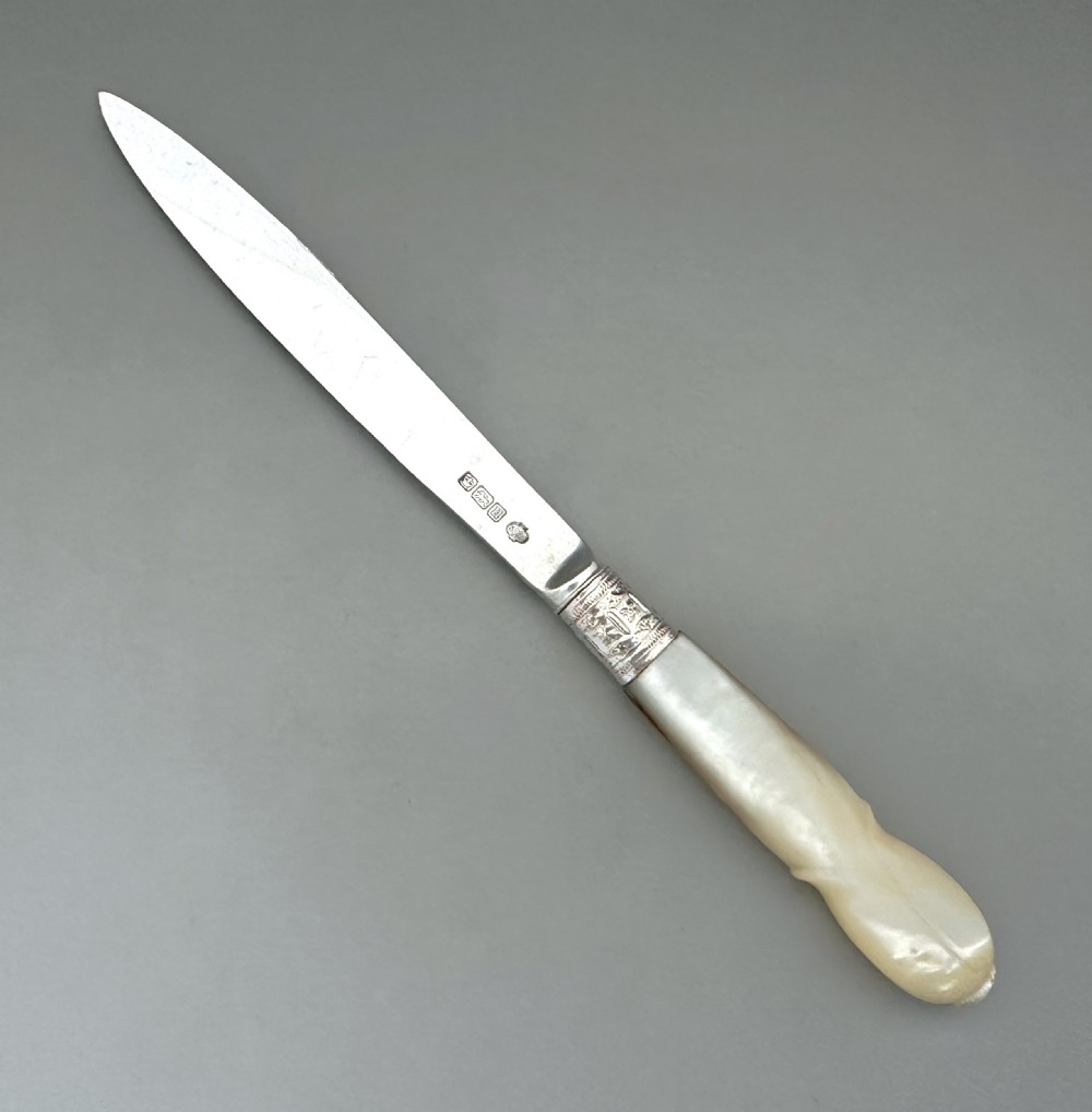 An antique George V letter opener featuring a tapered silver blade, an engraved silver collar, and a carved mother-of-pearl handle. View IV