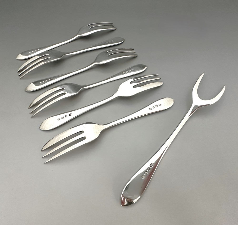 A cased set of six sterling silver cake forks and a central serving fork arranged in a black velvet-lined presentation box with a cream silk lid lining. View VIII