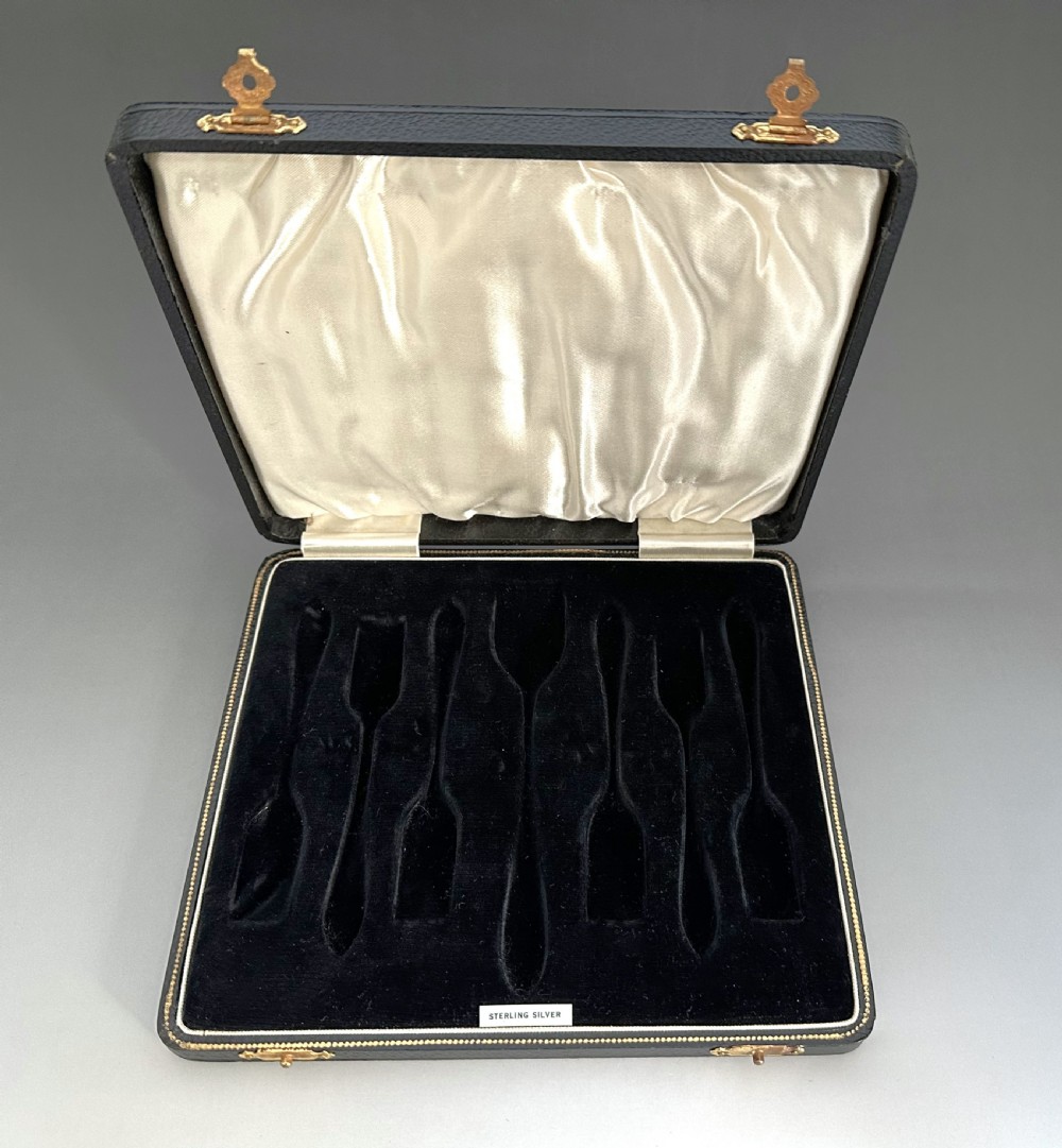 A cased set of six sterling silver cake forks and a central serving fork arranged in a black velvet-lined presentation box with a cream silk lid lining. View IX
