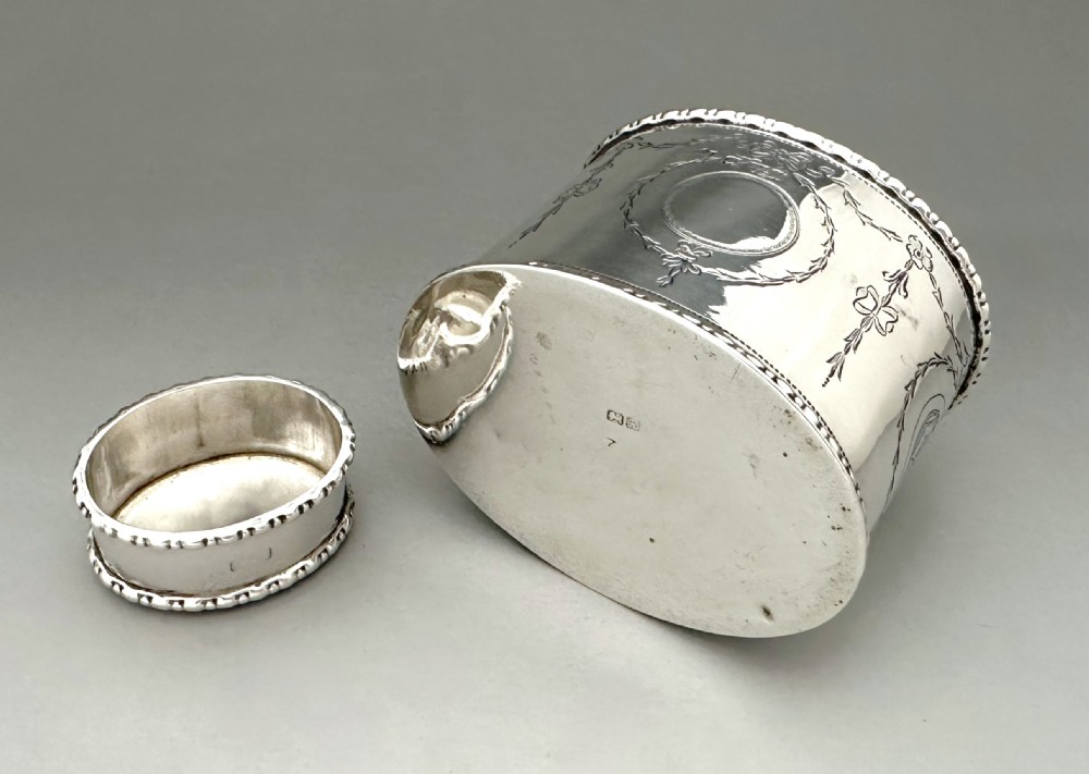 An oval sterling silver tea caddy featuring engraved floral garlands, ribbon swags, a vacant cartouche, and beaded borders. View VII