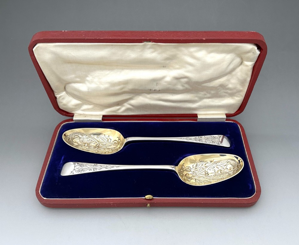 A pair of Art Nouveau sterling silver serving spoons with engraved foliate bowls and gold gilding, displayed in a red fitted velvet case. View II