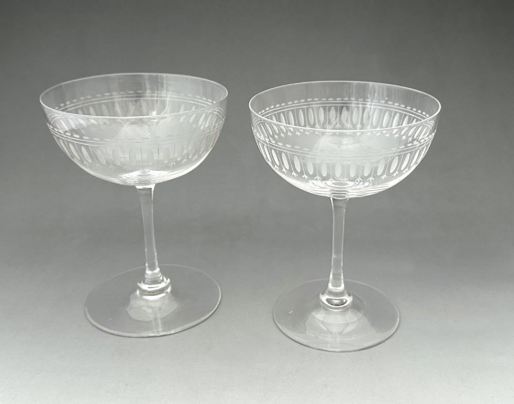 A pair of clear glass Victorian champagne coupes featuring etched geometric border decorations and slender stems.