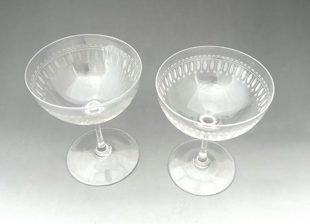 A pair of clear glass Victorian champagne coupes featuring etched geometric border decorations and slender stems. View II