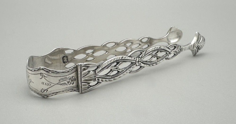A pair of 18th-century cast sterling silver sugar tongs featuring openwork pierced lattice arms and shell-shaped grips. View II