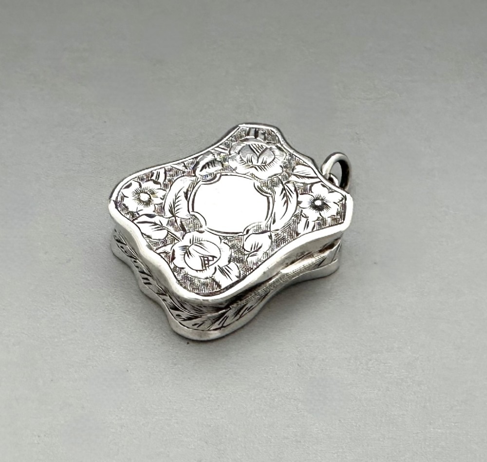 A shaped Victorian sterling silver vinaigrette with hand-engraved floral foliage, a central unengraved cartouche, and a side suspension ring.