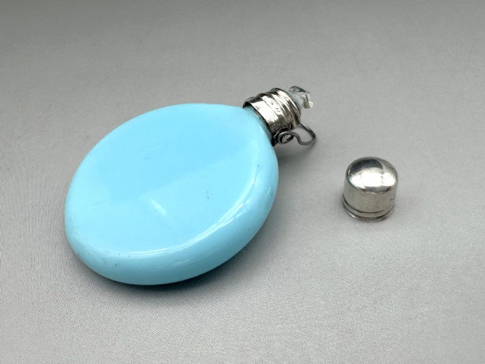 A circular light blue opaline glass scent bottle with a silver collar and hinged lid resting flat. View VI