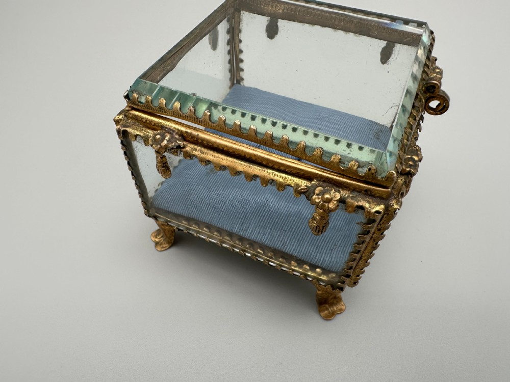 A square 19th-century French ormolu jewellery casket featuring bevelled glass panels, an ornate gilt frame with floral detailing, and a pale blue button-tufted silk interior. View VII