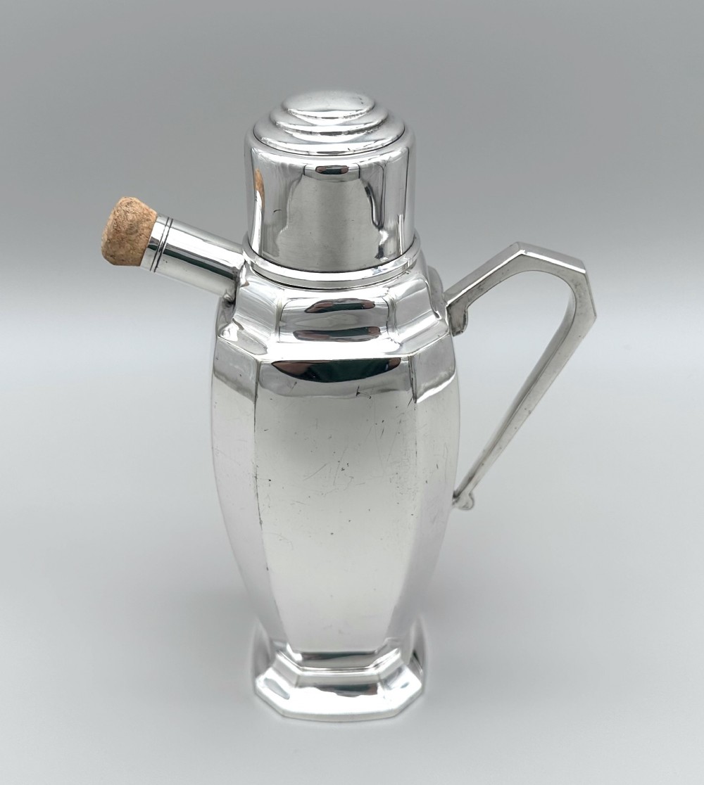 A polished silver-plated Art Deco cocktail shaker featuring an angular handle, stepped lid cap, and cork-capped spout.
