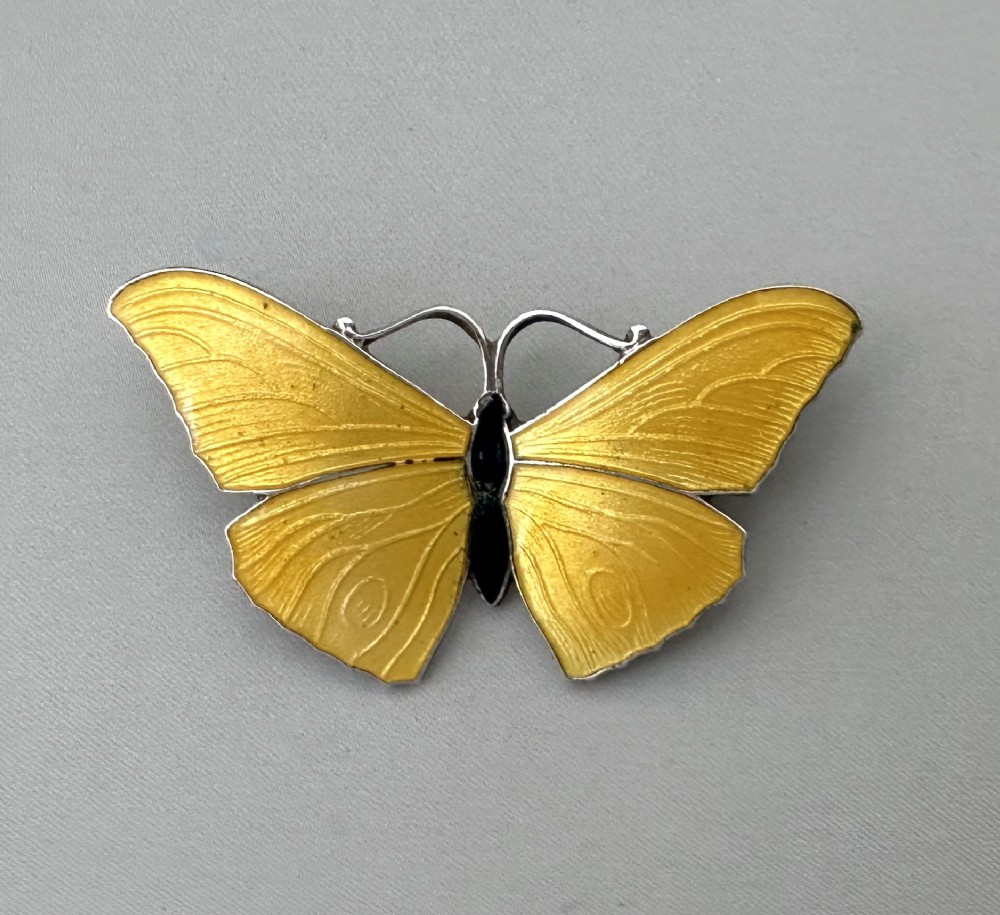 A silver butterfly brooch featuring yellow guilloche enamel wings and a dark central body.