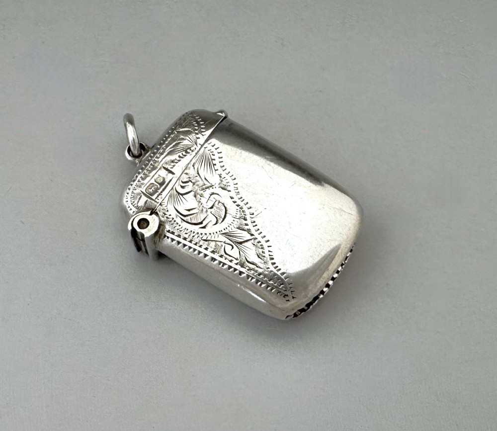 A small rectangular sterling silver vesta case featuring hand-engraved foliate decoration, a hinged lid, a suspension loop, and a serrated striker base. View II