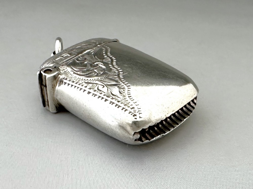 A small rectangular sterling silver vesta case featuring hand-engraved foliate decoration, a hinged lid, a suspension loop, and a serrated striker base. View III