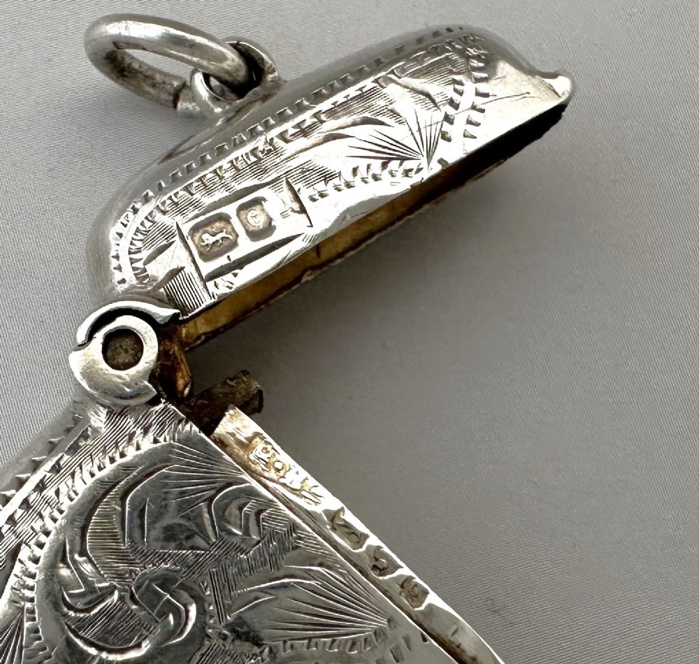 A small rectangular sterling silver vesta case featuring hand-engraved foliate decoration, a hinged lid, a suspension loop, and a serrated striker base. View V