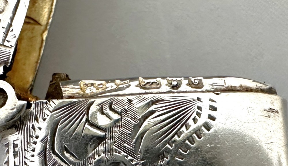 A small rectangular sterling silver vesta case featuring hand-engraved foliate decoration, a hinged lid, a suspension loop, and a serrated striker base. View VI
