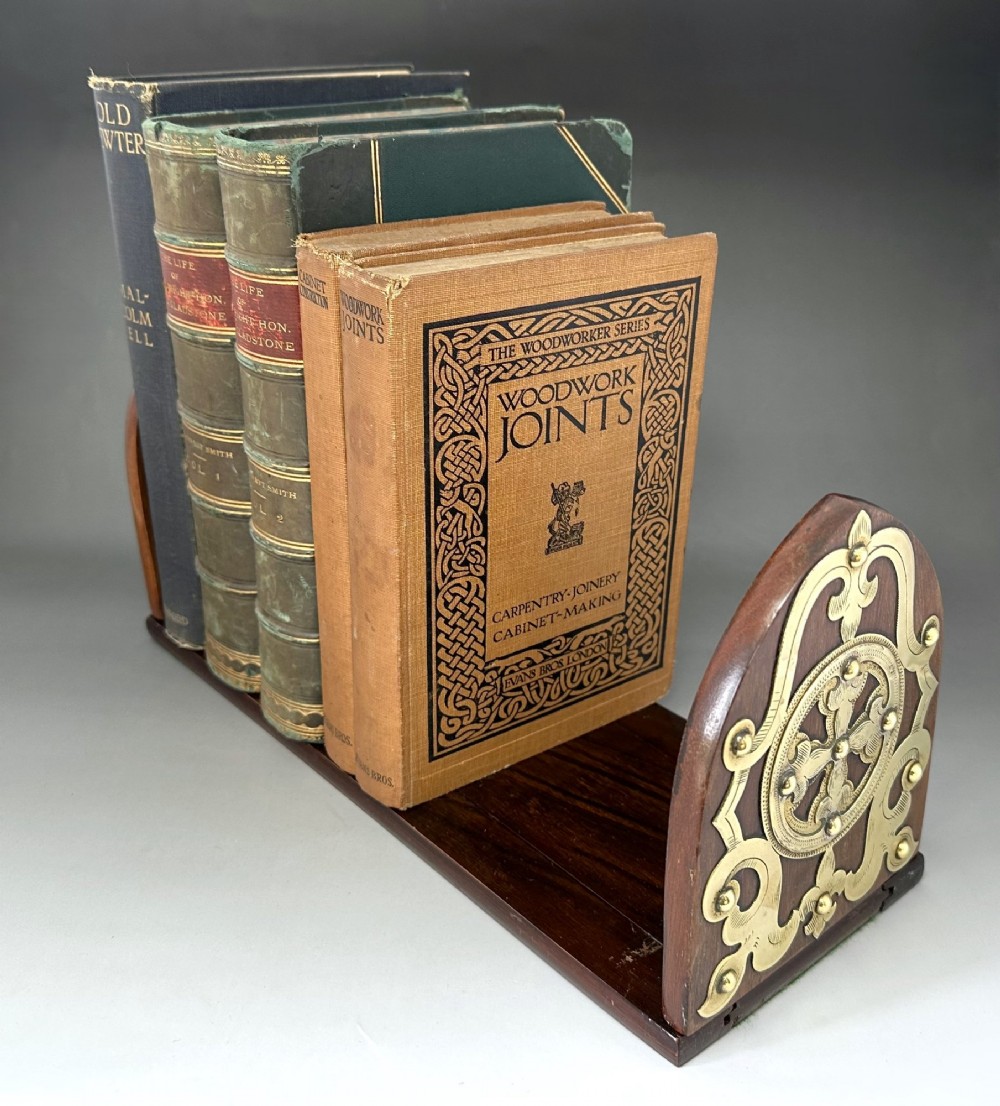 An extended wooden Victorian book slide with brass strapwork end panels holding a row of antique books.